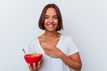 Young mixed race woman eating cereals isolated on white background laughs out loudly keeping hand on chest.