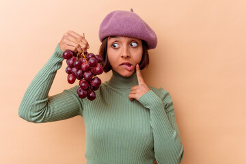 Young mixed race woman holding grapes isolated on beige background