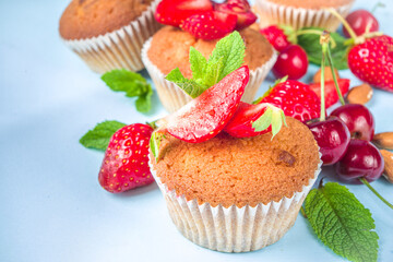 Summer baking concept, homemade vanilla white muffins with berry - strawberry, cherry, and mint, on baking sheet, light blue background top view copy space