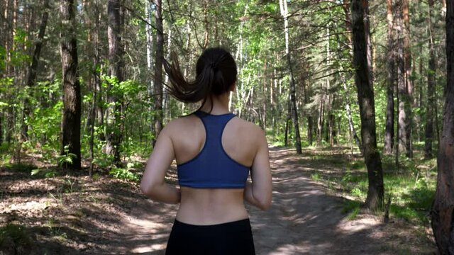 Sportive woman is engaged in fitness, runs on the road in a green park with trees. Running through the woods. Healthy body and mental health. Slow motion.