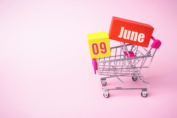 June 9th. Day 9 of month, Calendar date. Close up toy metal shopping cart with red and yellow box...