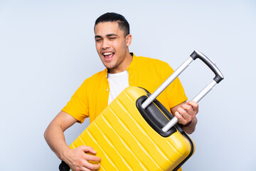 Asian handsome man isolated on blue background in vacation holding a travel suitcase like a guitar