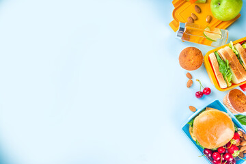 Back to school, Healthy tasty kid lunch box with sandwiches, nuts, fresh fruits and vegetable sticks. With school supplies, pencils, notebooks, on bright blue background flatlay top view copy space