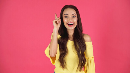 Fototapeta premium smiling young adult woman in yellow blouse pointing with finger isolated on pink