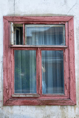 An old window with a dark pink wooden frame on the stone wall.