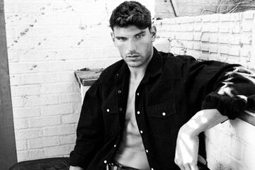 Portrait of handsome serious young man looking at camera with open black shirt revealing muscular...