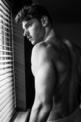 Black and white portrait of handsome topless man showing muscular arms, shoulders and back.