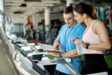 Personal trainer and athletic woman going through training plan during gym workout.