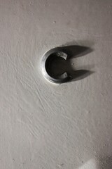 Capital letter C cast in metal and in a strong shadow.