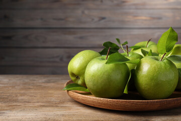 Fresh ripe green apples and leaves with plate on wooden table. Space for text