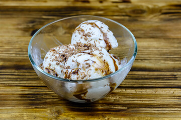 Glass bowl with ice cream balls and chocolate topping on a wooden table