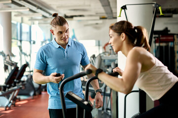 Young personal trainer using stopwatch during sports training with athletic woman in a gym.