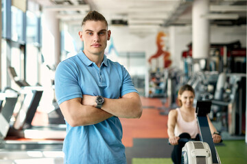 Fototapeta na wymiar Portrait of confident personal trainer with woman exercising in the background at the gym.
