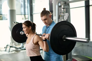 Poster Young athletic woman exercising with barbell with help of personal trainer in a gym. © Drazen
