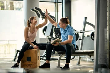Gordijnen Happy sportswoman and her personal trainer giving high-five after sports training in a gym. © Drazen