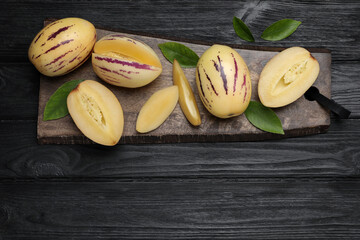 Whole and cut pepino melons with green leaves on black wooden table, top view. Space for text