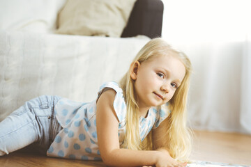 Happy family. Blonde young mother reading a book to her cute daughter while sitting at wooden floor. Motherhood concept