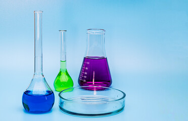 Three glass medical laboratory flasks with different multi-colored liquids and a glass bowl on a gentle blue medical background. The concept of medical and chemical experiments. Close-up. copy space.