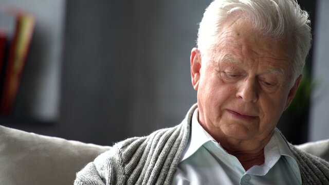Close up portrait of pensive elderly s man sit on couch in living room