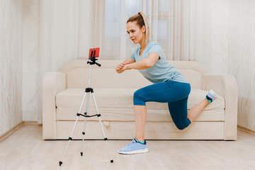 Fototapeta na wymiar Sportswoman using camera on tripod for streaming online fitness exercises, work as a trainer from home online remote, recording a video lesson, modern technologies and quarantine