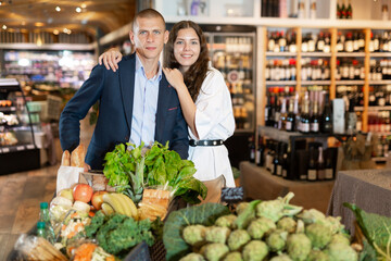 Portrait of young woman and man with shopping cart at vegetables department at supermarket