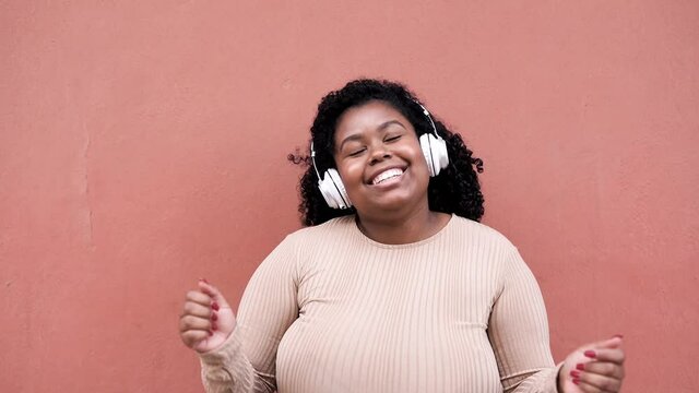 Young curvy african woman dacing to music playlist while wearing headphones - Concept of lifestyle and happiness
