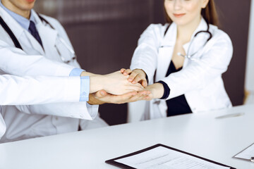 Obraz premium Group of doctors joining hands as a circle and ready to help patients while sitting at the desk in modern hospital office. Successful teamwork in medicine, Coronavirus countering concept