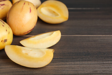 Cut pepino melon on wooden table, space for text