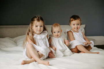 Close-up of happy children in room and looking at camera. Three little girls dressed in white...