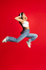 Asian woman with headphones jumping over red studio background with copyspace