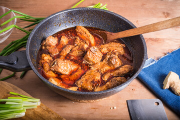 Spicy braised pork belly with pork ribs in a large wok on a wooden table - Thai, Chinese cuisine