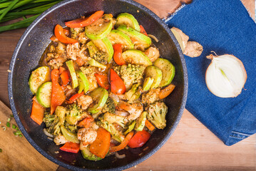 Stewed vegetables in a large frying pan on the table with ingredients - vegetarian healthy cuisine