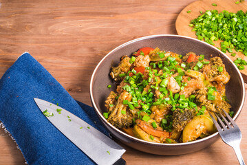 Stewed vegetables in a plate on a table with green onions on a cutting board, copy space - vegetarian healthy cuisine