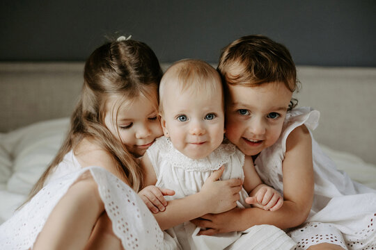 Front view of three cute little girls hugging together and looking at camera. Concept of happy childhood.
