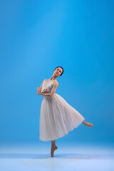Fototapeta na wymiar Young and incredibly beautiful ballerina is posing and dancing at blue studio full of light.