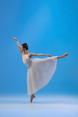 Fototapeta premium Young and incredibly beautiful ballerina is posing and dancing at blue studio full of light.