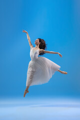 Young and graceful ballet dancer isolated on blue studio background. Art, motion, action, flexibility, inspiration concept.