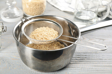 Sieve with rice in pot on grey wooden table