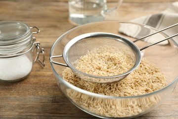 Sieve with rice in bowl on wooden table