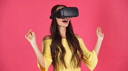 young adult woman in vr headset gesturing with hands in air isolated on pink