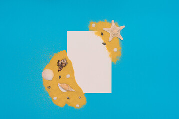 Different sea shells and starfish on bright yellow sand with white paper card note on blue background. Summer time concept. Flat lay style with copy space 