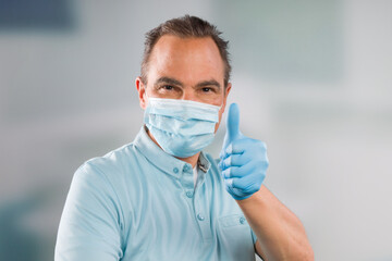 Doctor with medical face mask and medical gloves shows thumbs up