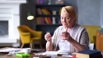 senior woman with glass of water taking pills at home