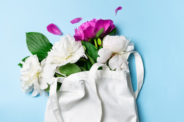 Reusable white lien bag with aromatic peony flowers on light blue background top view. Eco shopping concept. Flowers delivery banner.
