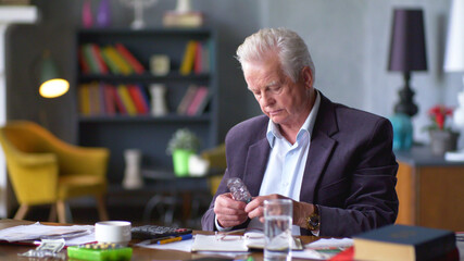 Senior man with cup of water and pill taking remedy in cozy room at home