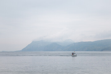 A boat sailing through the bay of Santoña, Cantabria, a cold and cloudy day with fog.