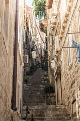 A narrow street in Dubrovnik, Croatia, with ascending stairs and a pleasant shade that forms between the buildings at midday.