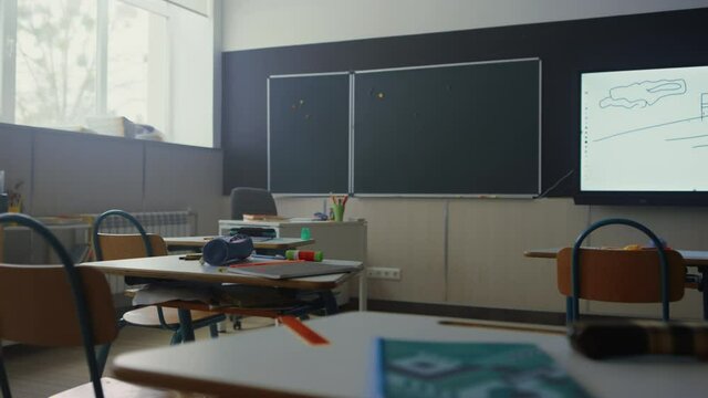 School classroom with chalkboard. School desks and chairs with supplies