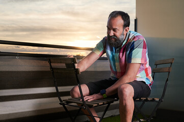 portrait of a middle-aged man sanding a chair on his terrace during a beautiful sunset.