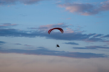 The paraglider flies high in the sky. Paraglider on the background of the sunset sky. The concept of extreme sports.